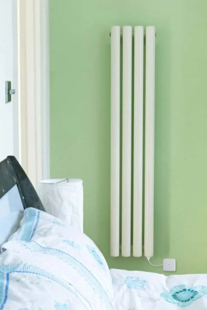 Modern white radiator for home heating on light green wall.