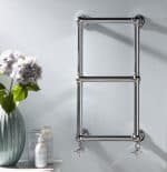 Polished chrome towel radiator in modern bathroom, wall mounted with valves.