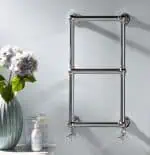 Polished chrome towel radiator in modern bathroom, wall mounted with valves.