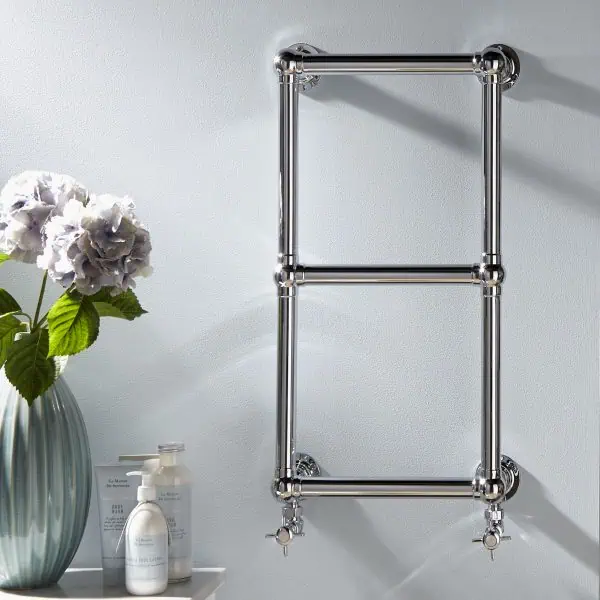Polished chrome towel radiator in modern bathroom, wall mounted with valves.