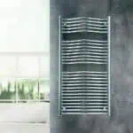 Shiny chrome towel radiator mounted on grey wall in modern bathroom.