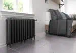 Black cast iron radiator near a window with bedding on a bed frame; heating solutions for modern homes.