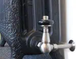 Vintage black cast iron radiator with silver tap detail for heating and decoration.