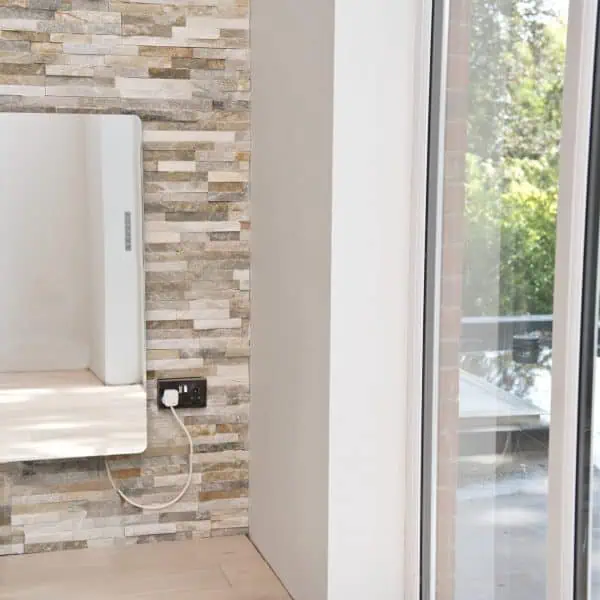 Modern electric radiator with sleek design mounted on stone feature wall in a bright, contemporary home interior.