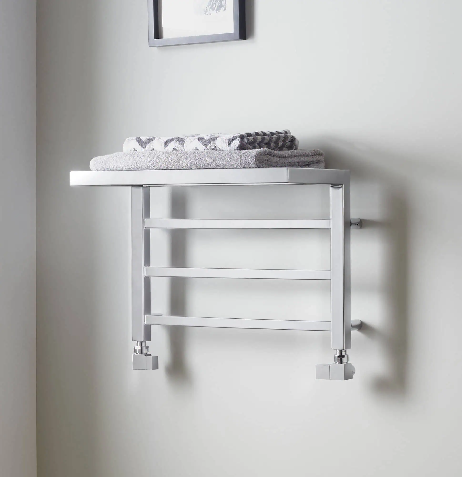 Shower towel radiator installed on a bathroom wall with neatly folded towels on top.