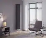 Modern vertical black radiator in stylish living room corner with large window and armchair.