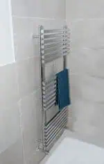 Polished chrome towel radiator in modern bathroom wall.