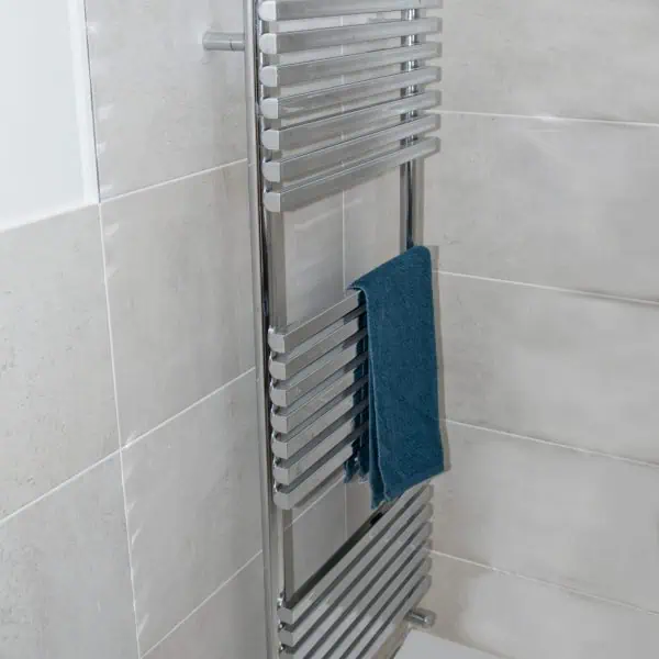 Polished chrome towel radiator in modern bathroom wall.