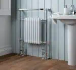 Radiator and piping installation in a modern bathroom, featuring chrome fixtures and wall paneling.