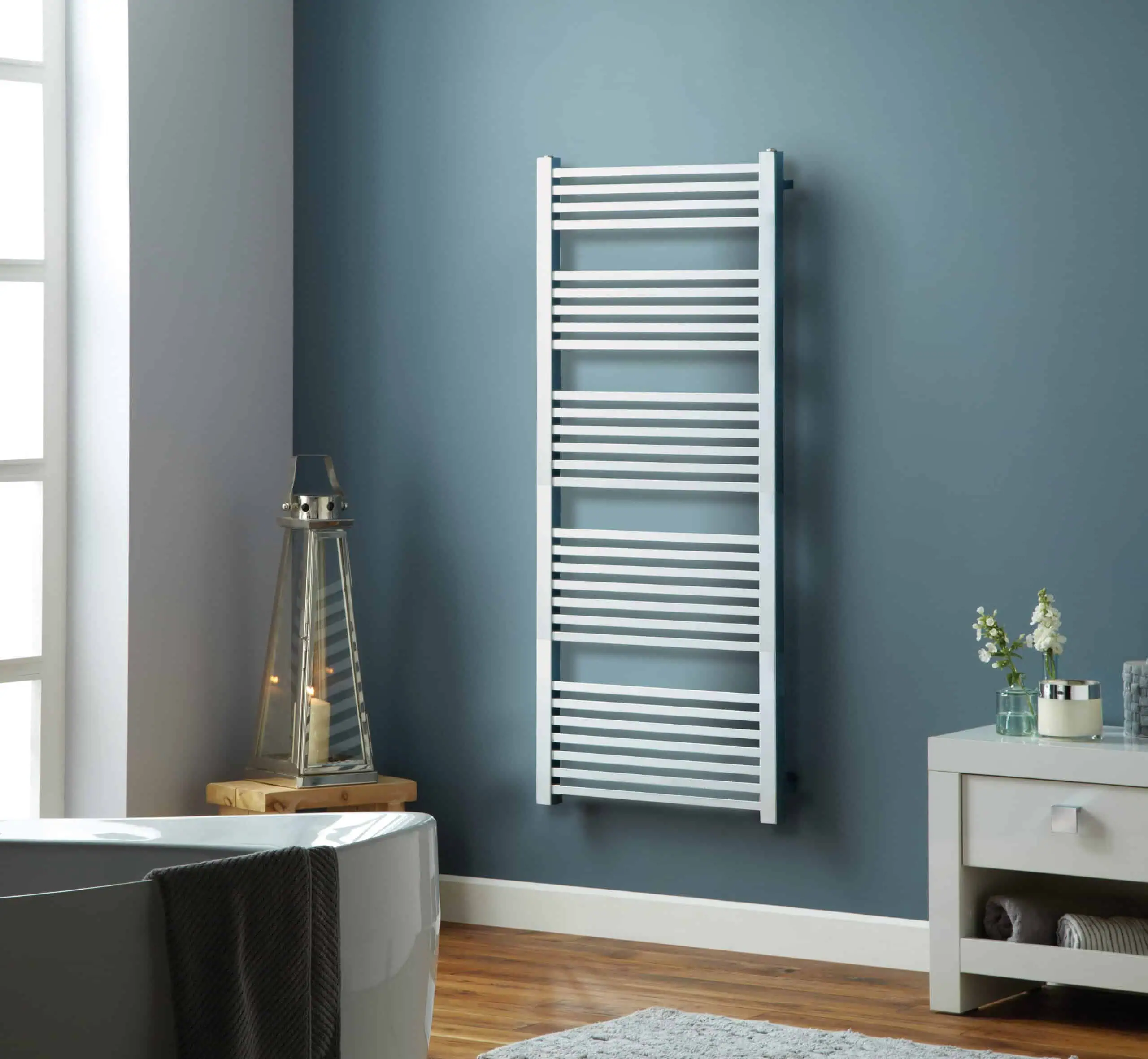Square-Chrome-1600x600-Lifestyle-rgb-scaled-2.jpg White heated towel rack on blue wall in modern bathroom.