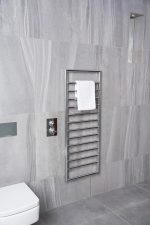 Chrome towel radiator heater in modern bathroom with gray tiles, heated towel rail for comfort.
