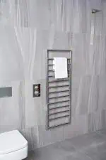 Chrome towel radiator heater in modern bathroom with gray tiles, heated towel rail for comfort.