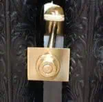 High-security door latch with brass lock and ornate black wooden door.