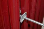 High-quality door hardware bolt with adjustable steel rod, red wooden door, secure locking mechanism.