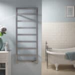Chrome towel radiator in modern bathroom with clawfoot bathtub and white brick wall.