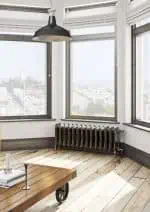 Bright modern interior with large windows, radiator, wooden flooring, and industrial-style pendant light.