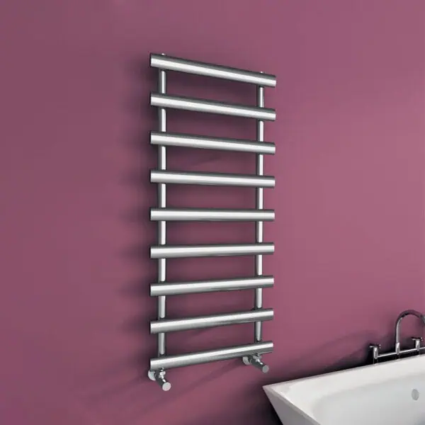 Stainless steel heated towel rail mounted on pink wall in modern bathroom.