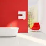 Modern bathroom with freestanding bathtub and vibrant red accent wall, minimalist interior design, natural light, and scenic view outside window.