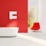 Modern bathroom with freestanding white tub, red accent wall, and contemporary red lounge chair. Bright, minimalist interior design.
