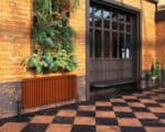 Modern indoor garden wall with lush green plants and black grid backdrop, stylish radiator and brick wall interior.