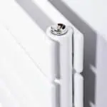 Radiator close-up with chrome screw and white panel, modern heating system design.