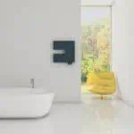 Modern bathroom with freestanding bathtub, black radiator, and yellow lounge chair in bright space with large window.