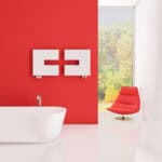 Modern bathroom interior with red accent wall, white bathtub, and stylish lounge chair, bright natural light.