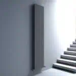 Sleek black modern radiator mounted on a gray wall near staircase, stylish home heating solution.