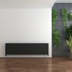 Modern sleek black radiator on a white wall with green plants in stylish interior setting.
