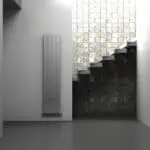 Radiator mounted on white wall with textured black and white brick wall background, modern minimalist interior design.