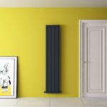 Black modern vertical radiator on yellow wall in contemporary interior.