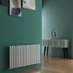Radiator under a green wall with framed artwork, stylish modern interior decor, warm wooden flooring.