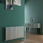 Radiator under a green wall with framed artwork, stylish modern interior decor, warm wooden flooring.