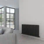 Modern black radiator installation inside a contemporary living room with large glass doors.