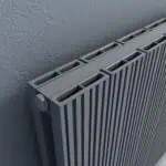 Modern gray radiator with vertical slats mounted on textured wall for home or office heating solutions.