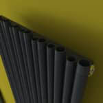 Black aluminum pipe radiator against yellow wall, modern heating solution, efficient home heating system.