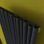 Black aluminum pipe radiator against yellow wall, modern heating solution, efficient home heating system.
