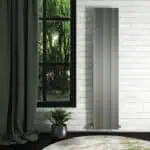 Modern vertical grey radiator in a minimalist interior setting with a large window and greenery outside.