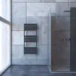 Modern bathroom with sleek gray towel radiator and glass shower partition, minimalist design, tiled walls and floors.