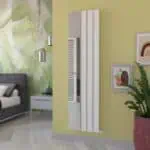 Modern white vertical radiator in a stylish living room with yellow accent wall and decorative artwork.