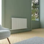 Radiator installation in modern green room with large window and wooden flooring.