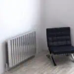 Radiator and modern black lounge chair in minimalist interior space, stylish home decor.