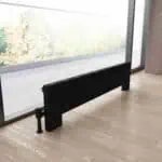Black modern radiator installed near a glass door in a contemporary living space.