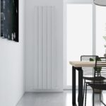 Modern vertical radiator in a minimalist dining room setting with black furniture and natural light.