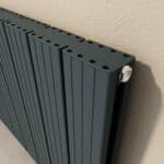 Modern black radiator with metal knob for temperature control, installed against textured beige wall.