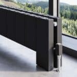 Radiator with modern black design near window overlooking green forest landscape.