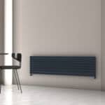Modern black radiator wall heater in a minimalist interior with a black chair and gray wall.