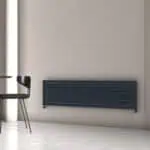 Modern black radiator wall heater in a minimalist interior with a black chair and gray wall.