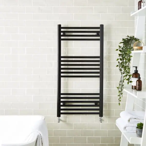 Modern black towel radiator in bathroom, wall-mounted, with chrome wheels, sleek and functional.