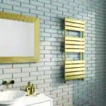 Polished gold towel radiator and modern bathroom decor with white brick wall and vanity, elegant bathroom design.